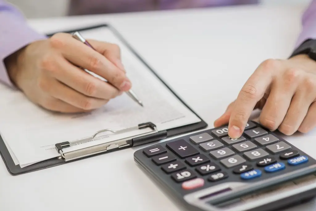 Pessoa usando calculadora e fazendo anotações em um papel fixo na prancheta