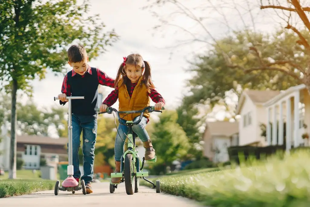 2 crianças, uma de bicicleta, outra de patinete, brincando na rua