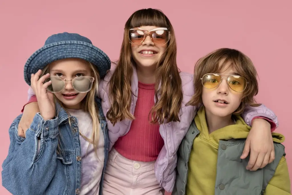 3 crianças de óculos abraçadas, fundo rosa