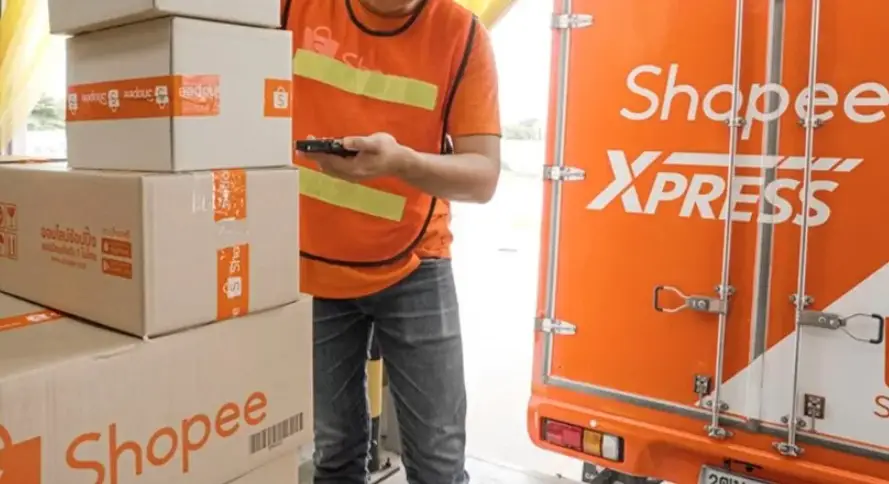 Homem com colete laranja empilhando caixas de papelão da shopee