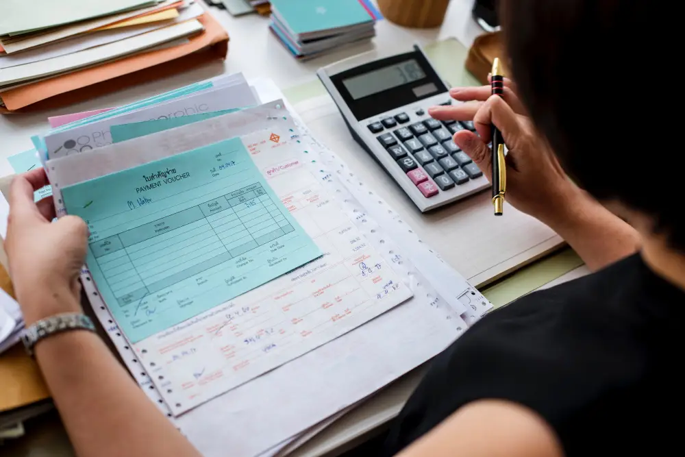 mulher olhando e segurando papeis , com a outra mão mexe na calculadora