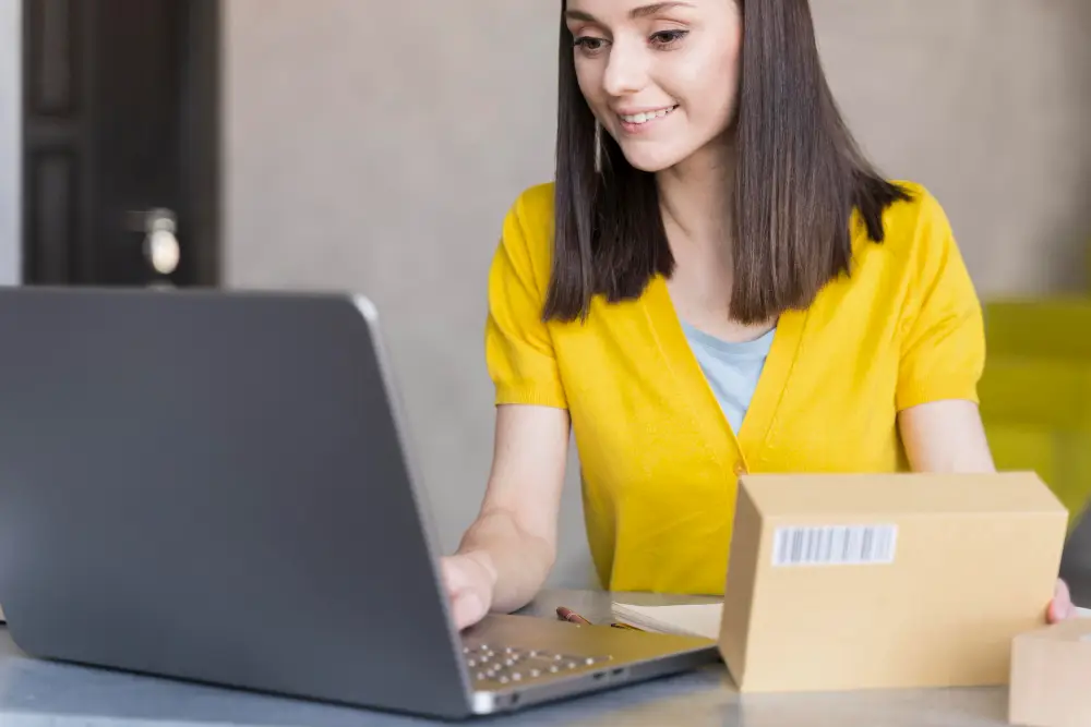 mulher mexendo no seu notebook e segurando uma caixa de encomenda