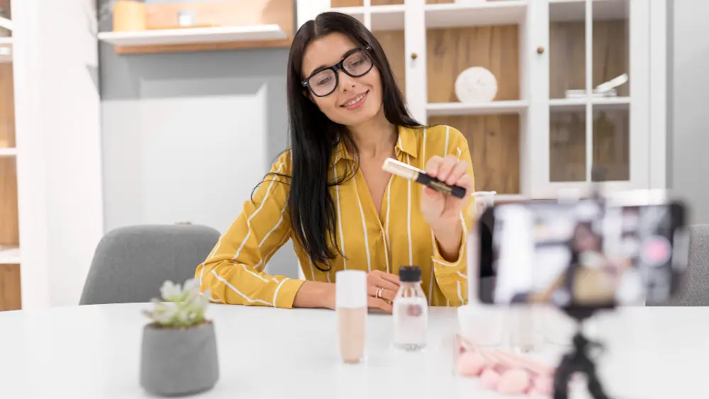 Mulher fazendo a gravação de um video, segurando um produto de beleza. Celular no tripe 