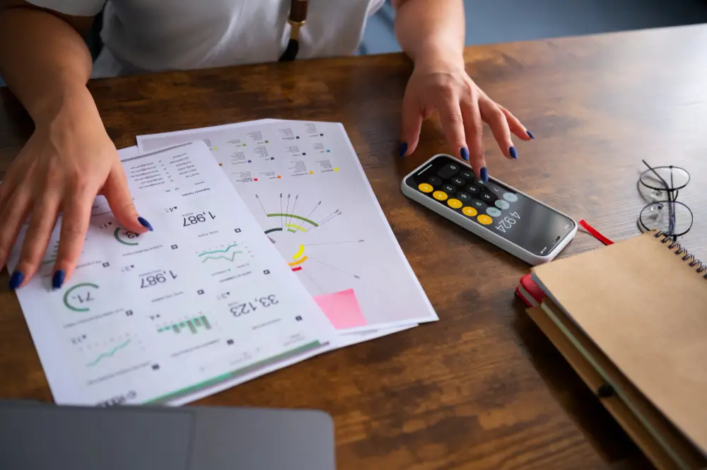 Relatório de fluxo de caixa sobre a mesa e mulher digitando na calculadora do celular